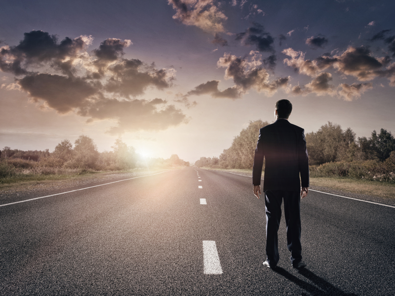 Homme d'affaires se tenant sur une route déserte, fixant l'horizon.