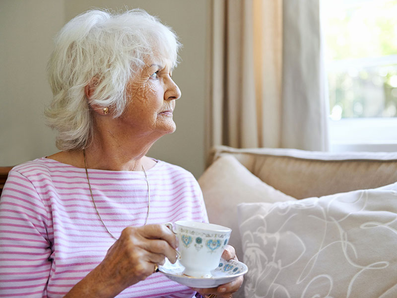 Femme âgée pensive, tenant une tasse de thé et regardant par la fenêtre.