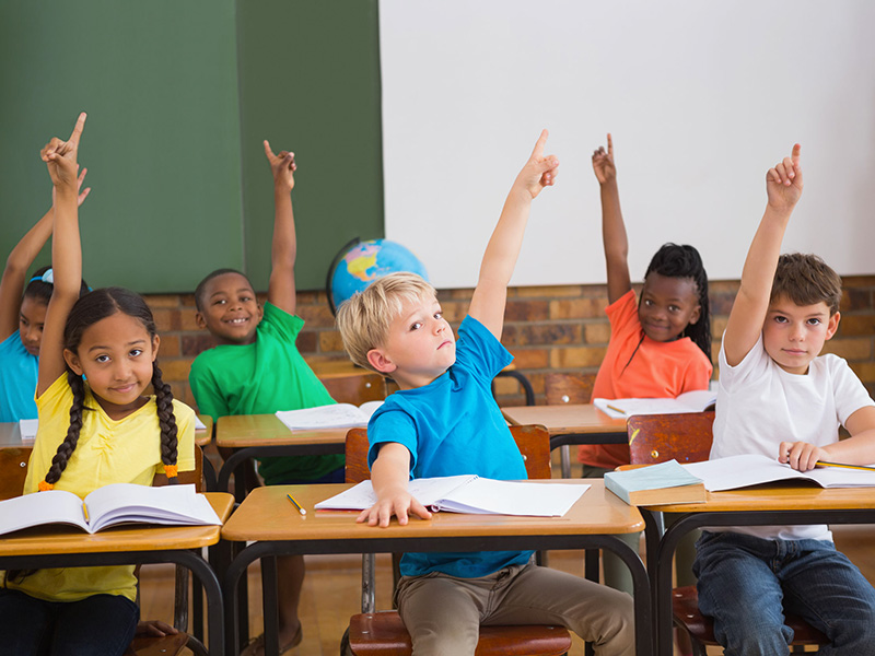 Enfants dans une salle de classe, la main levée.
