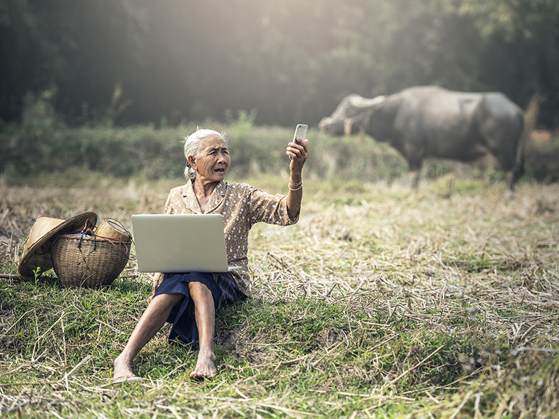 Femme âgée vietnamienne assise dans un champ et prenant un selfie.