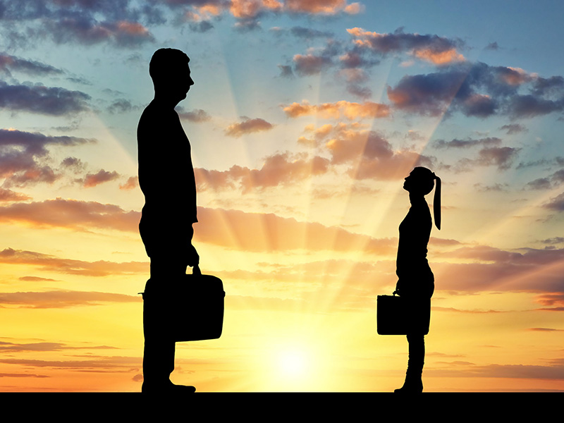 Un homme géant et une femme minuscule debout devant un coucher de soleil.