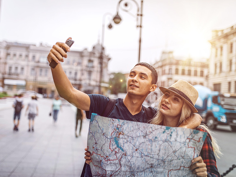 Jeune couple en voyage, tenant une carte routière et se prenant en selfie.