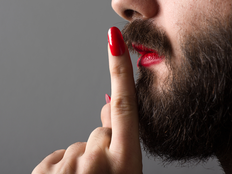 Homme portant du rouge à lèvres et du vernis à ongles faisant signe de rester silencieux.
