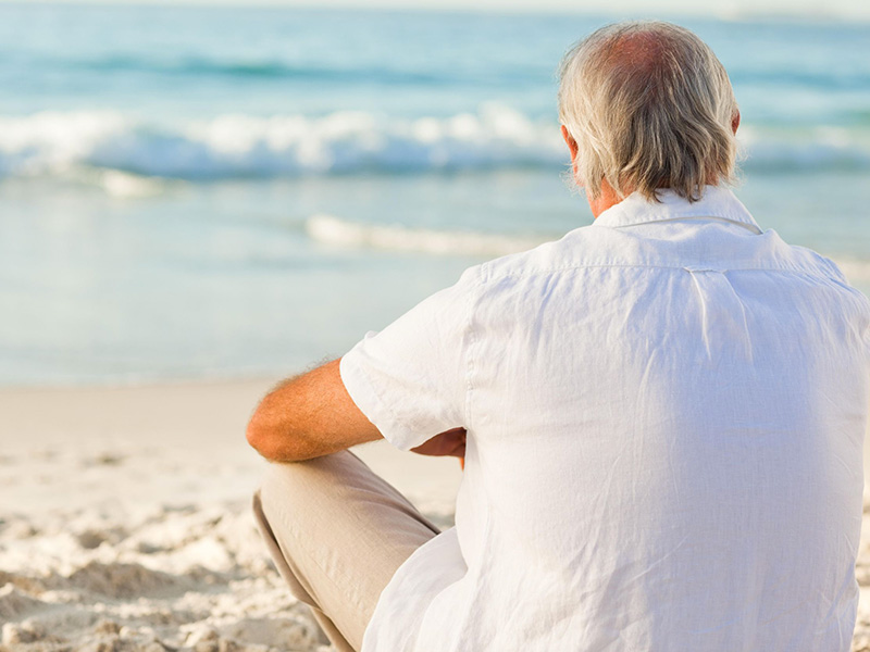 Homme retraité assis devant la mer.