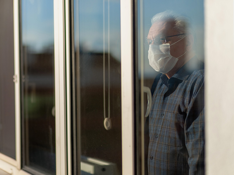 Homme âgé regardant par une fenêtre et portant un masque