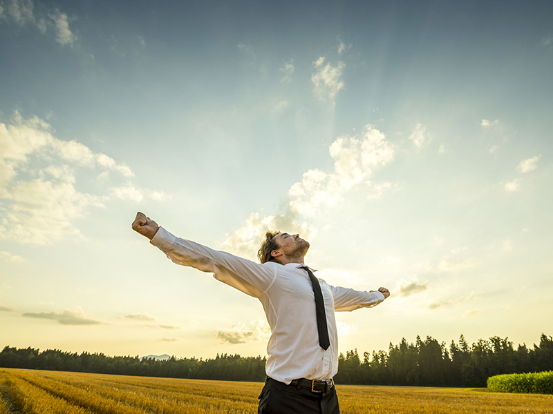 Homme d'affaires dans un champ de blé, levant les bras vers le ciel.