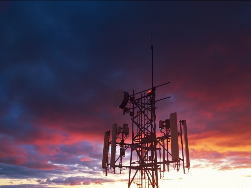 Une tour de télécommunication sur un fonds de ciel nuageux au coucher du soleil.