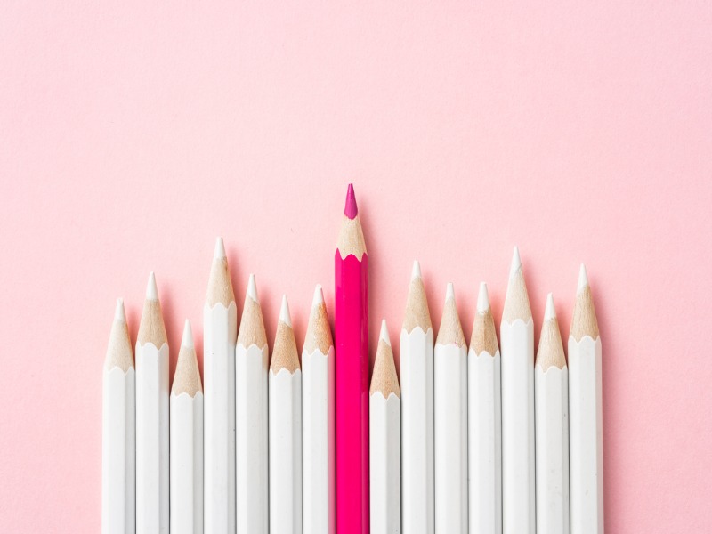 Rangée de crayons blancs avec un seul crayon rose qui se démarque.