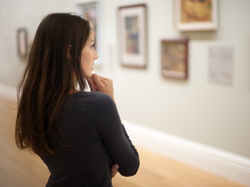 Une femme dans un musée en train de regarder des tableaux.