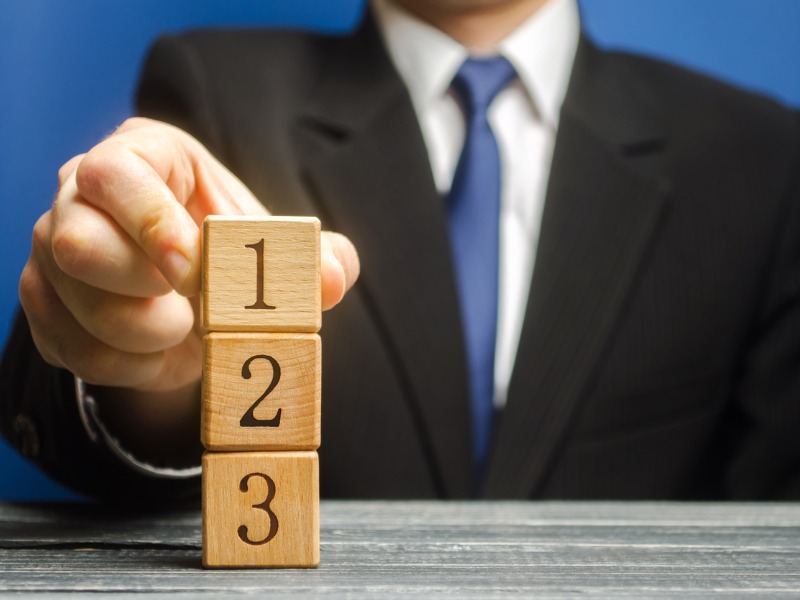 Un homme d'affaires posant un cube portant le numéro 1, sur une colonne de deux autres cubes portant le numéro 2 et 3.