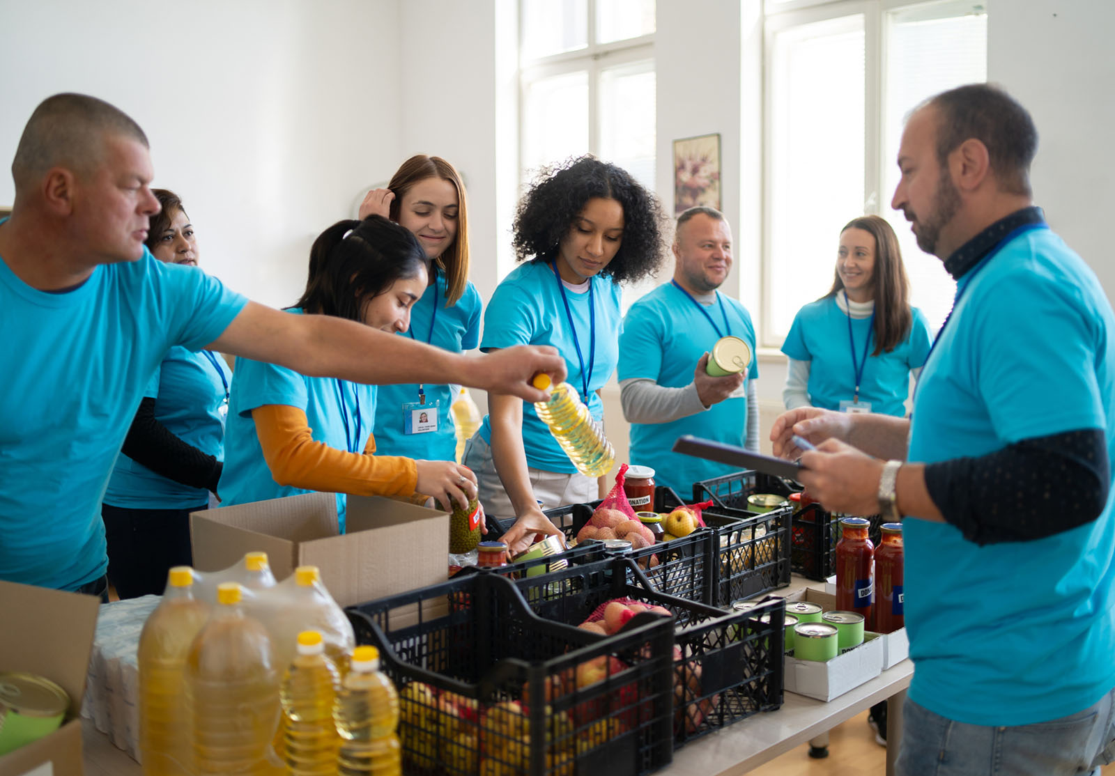 Des bénévoles multiraciaux, vêtus de t-shirts assortis, emballent des boîtes de dons alimentaires dans une banque alimentaire.