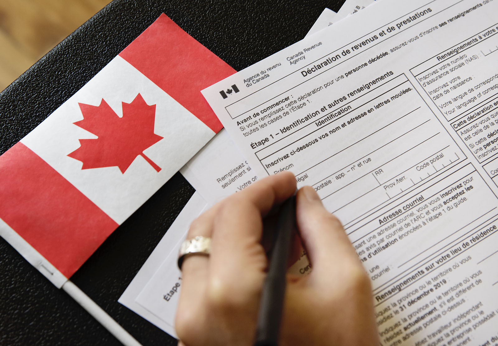 Un homme remplit à la main des documents fiscaux canadiens. Drapeau canadien sur la table. Gros plan horizontal à l'intérieur d'un espace de copie.
