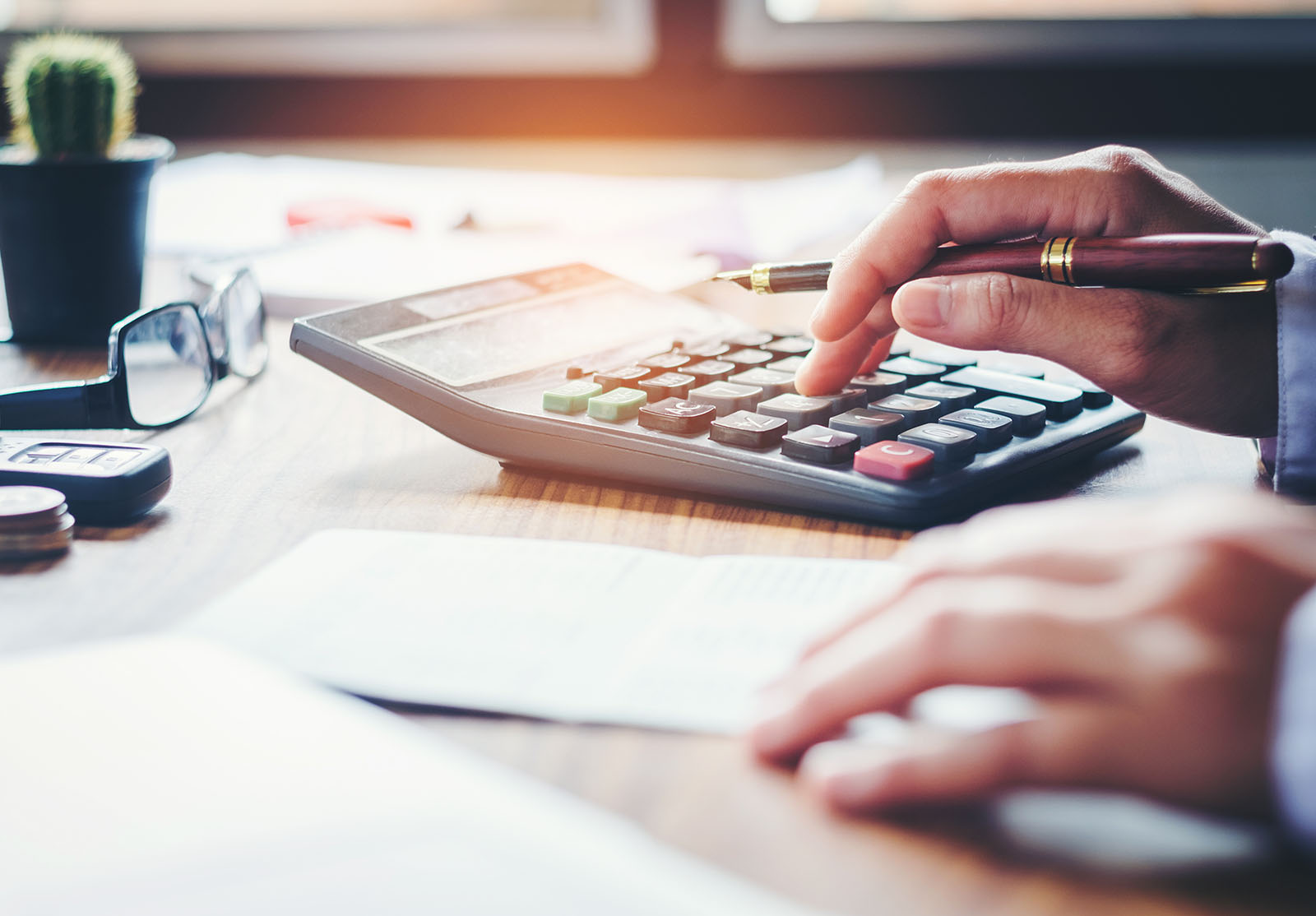 Les mains d'un homme d'affaires avec une calculatrice et un coût au bureau et des données financières analysant le comptage sur un bureau en bois.