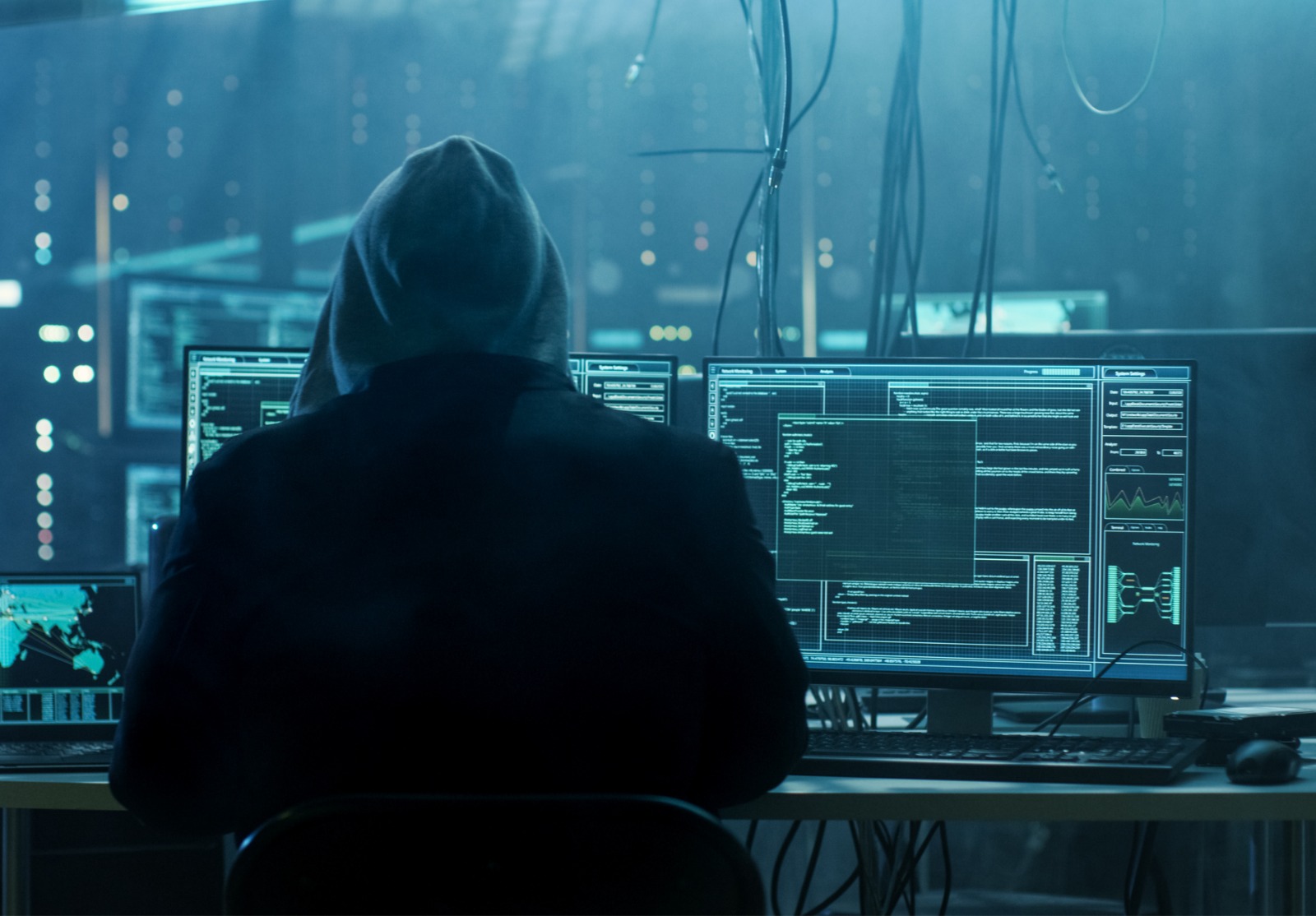 Dangereuse Hacker Hooded entonne des serveurs de données de gouvernement et infecte leur système avec un Virus. Son lieu de cachette a l’atmosphère sombre, plusieurs écrans, câbles partout.