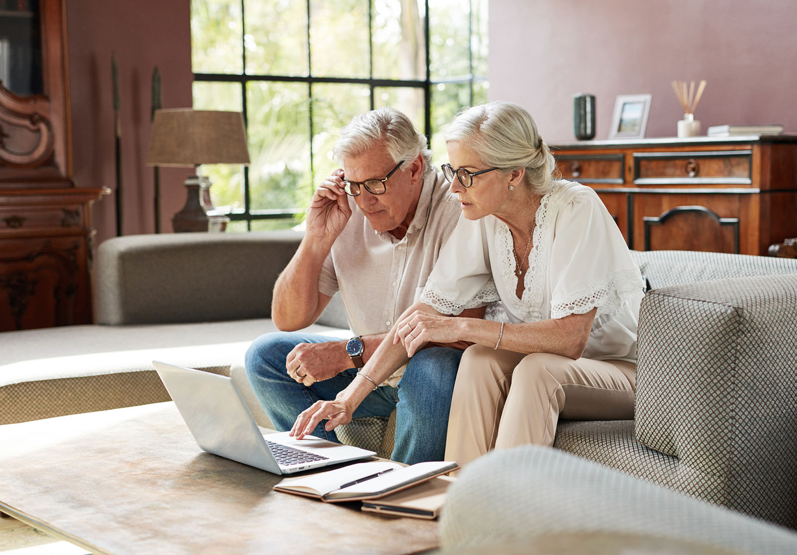 Vue d'un couple d'âge mûr utilisant un ordinateur portable tout en calculant leurs finances à la maison.