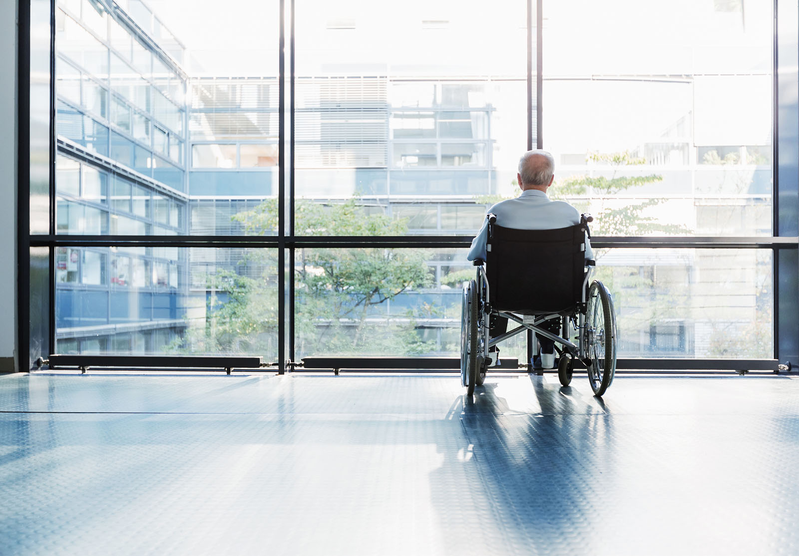 Homme âgé en fauteuil roulant regardant par la fenêtre dans un couloir d'hôpital.