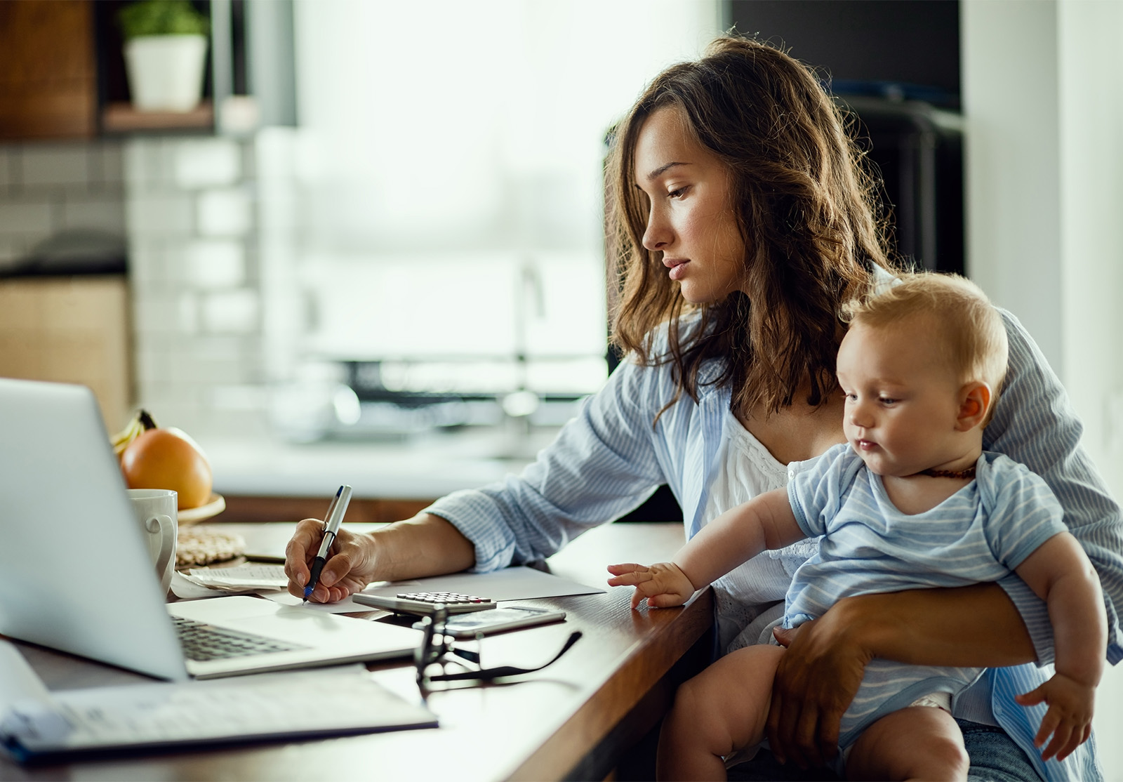 Femme équilibrant un bébé sur ses genoux alors qu'elle est assise devant un ordinateur portable